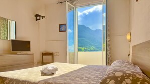 Ein Hotelzimmer mit Bett, Fernseher, Sessel und Blick auf Berge durch ein großes Fenster.