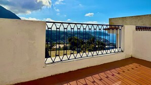 Ein Balkon mit Metallgeländer, Blick auf eine Küstenlandschaft und einen klaren Himmel.
