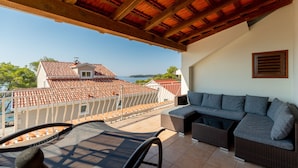 Un balcón con un sofá y sillones de mimbre, con vistas a una zona costera con tejados de teja.