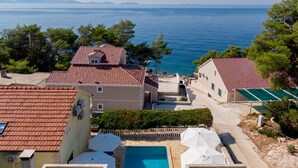 Un área residencial costera con casas de techo de tejas rojas, una piscina y vistas al mar.