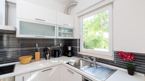 Una cocina moderna con gabinetes blancos, un lavamanos de acero inoxidable y una ventana con vista a zonas verdes.