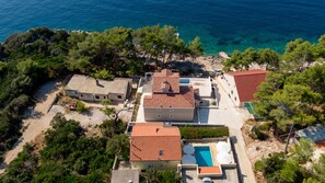 Vue aérienne d’une propriété côtière comprenant plusieurs bâtiments, une piscine et de la végétation luxuriante.