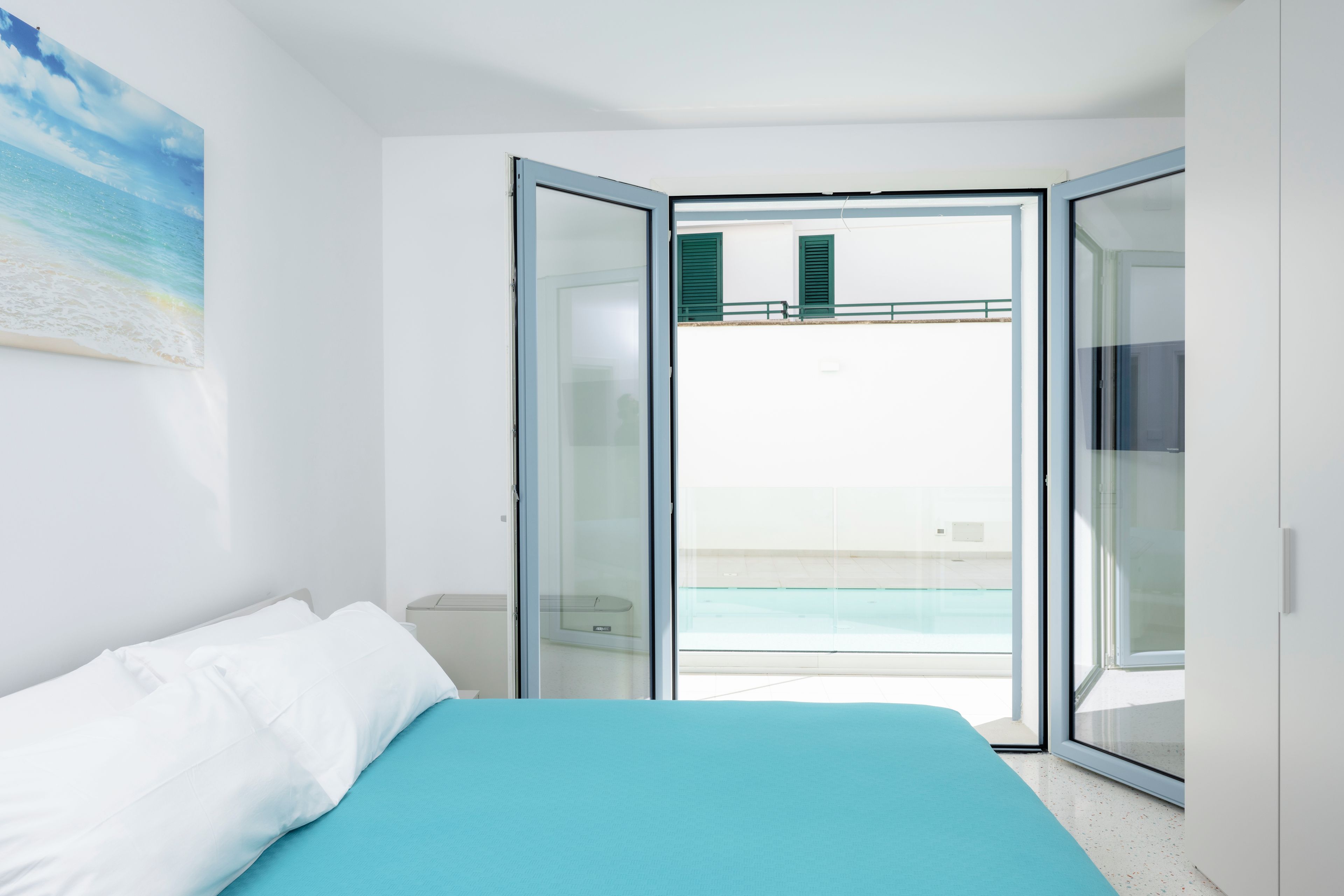 Quarto com cama, vista para uma piscina e varanda com persianas verdes.