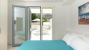 Quarto com cama, porta de vidro deslizante para uma varanda com m óveis de exterior.