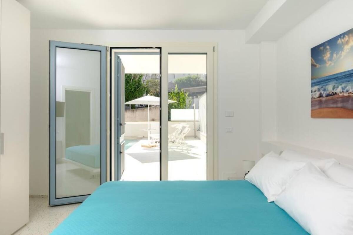 A bedroom with a bed, a sliding glass door leading to a balcony with outdoor furniture.