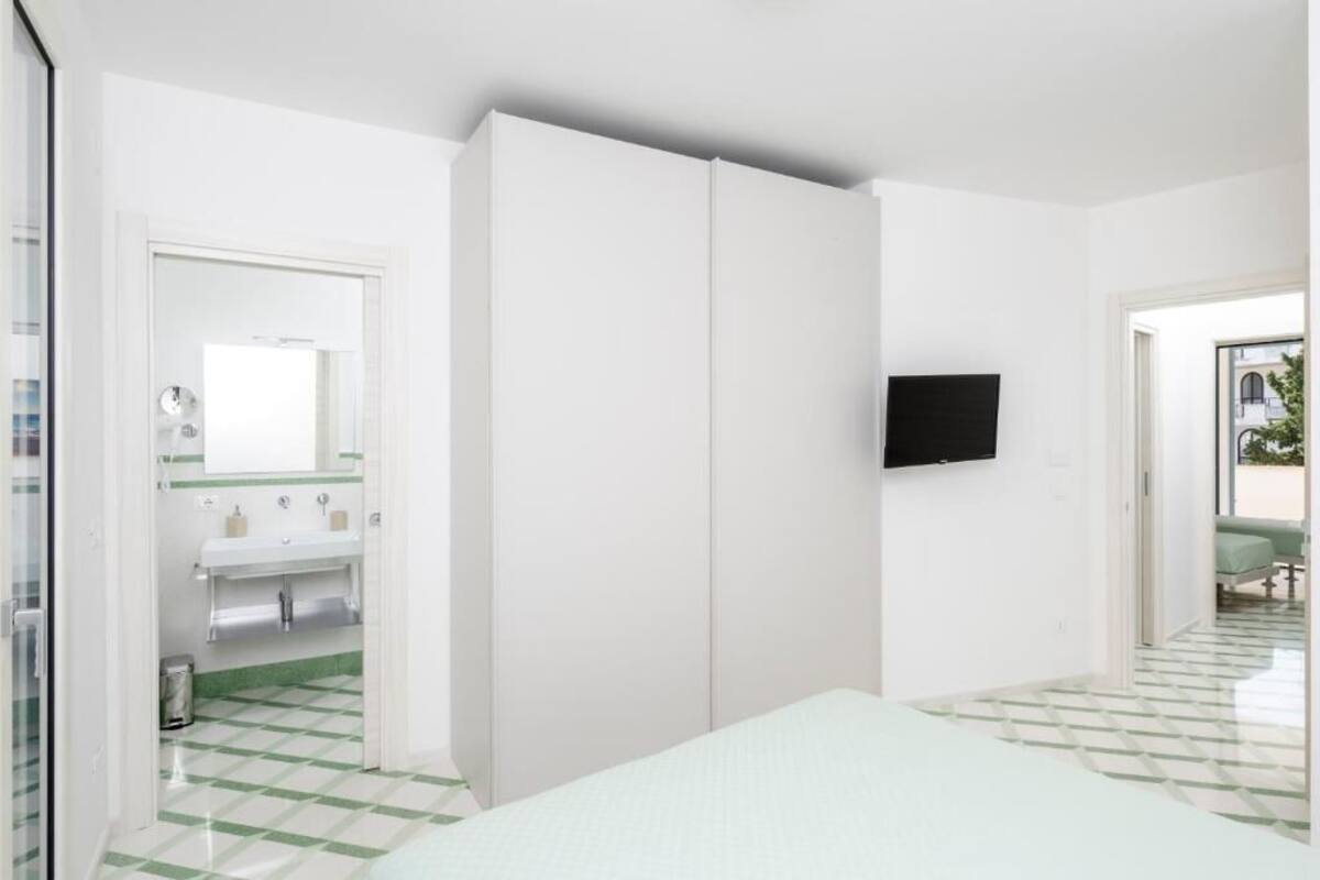 A bedroom with a bed, a TV mounted on the wall, and a bathroom with a sink and mirror.