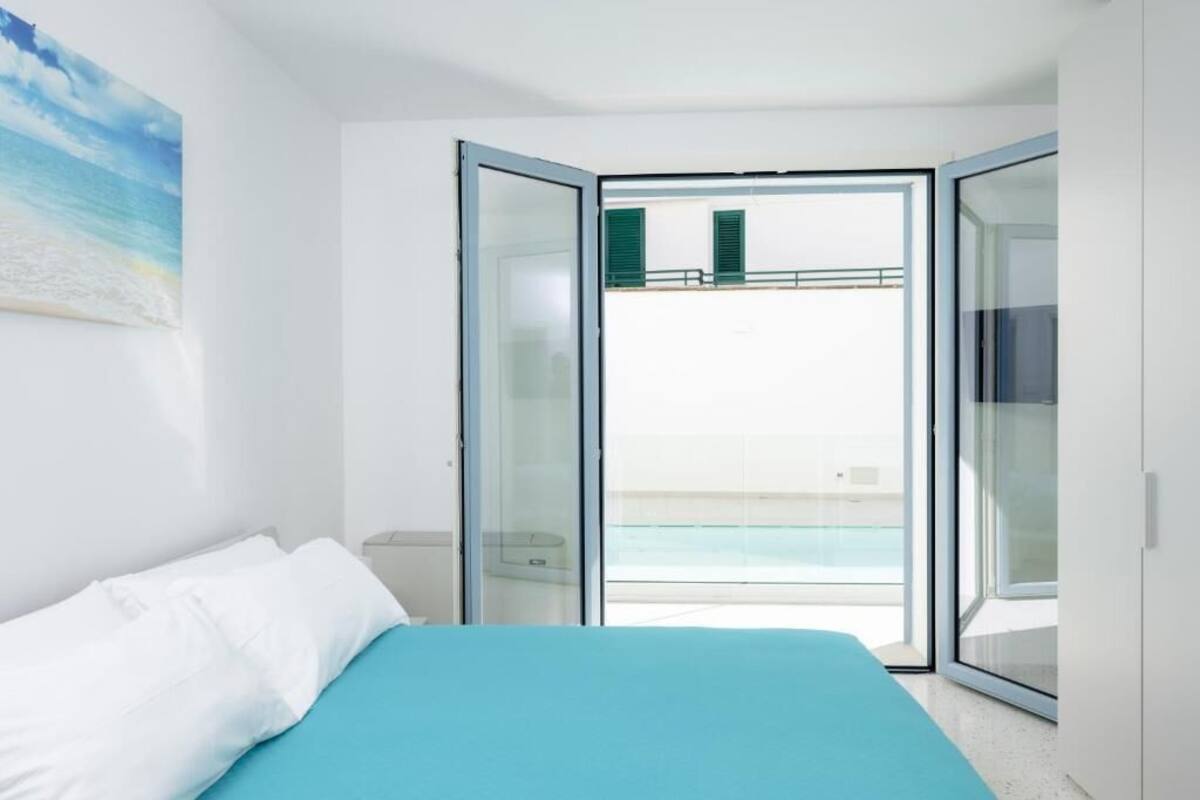 A bedroom with a bed, a painting, and a balcony with a pool view.