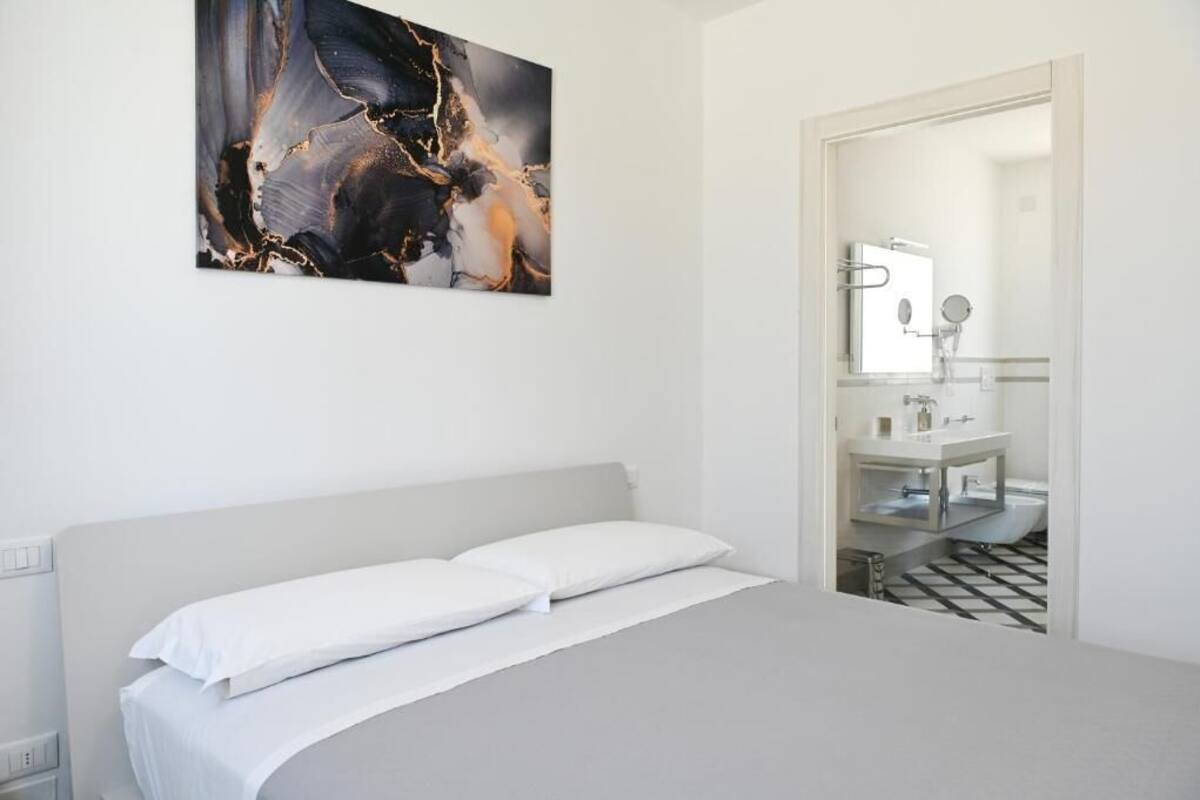 A bedroom with a bed, a white wall, and a bathroom visible through an open door.