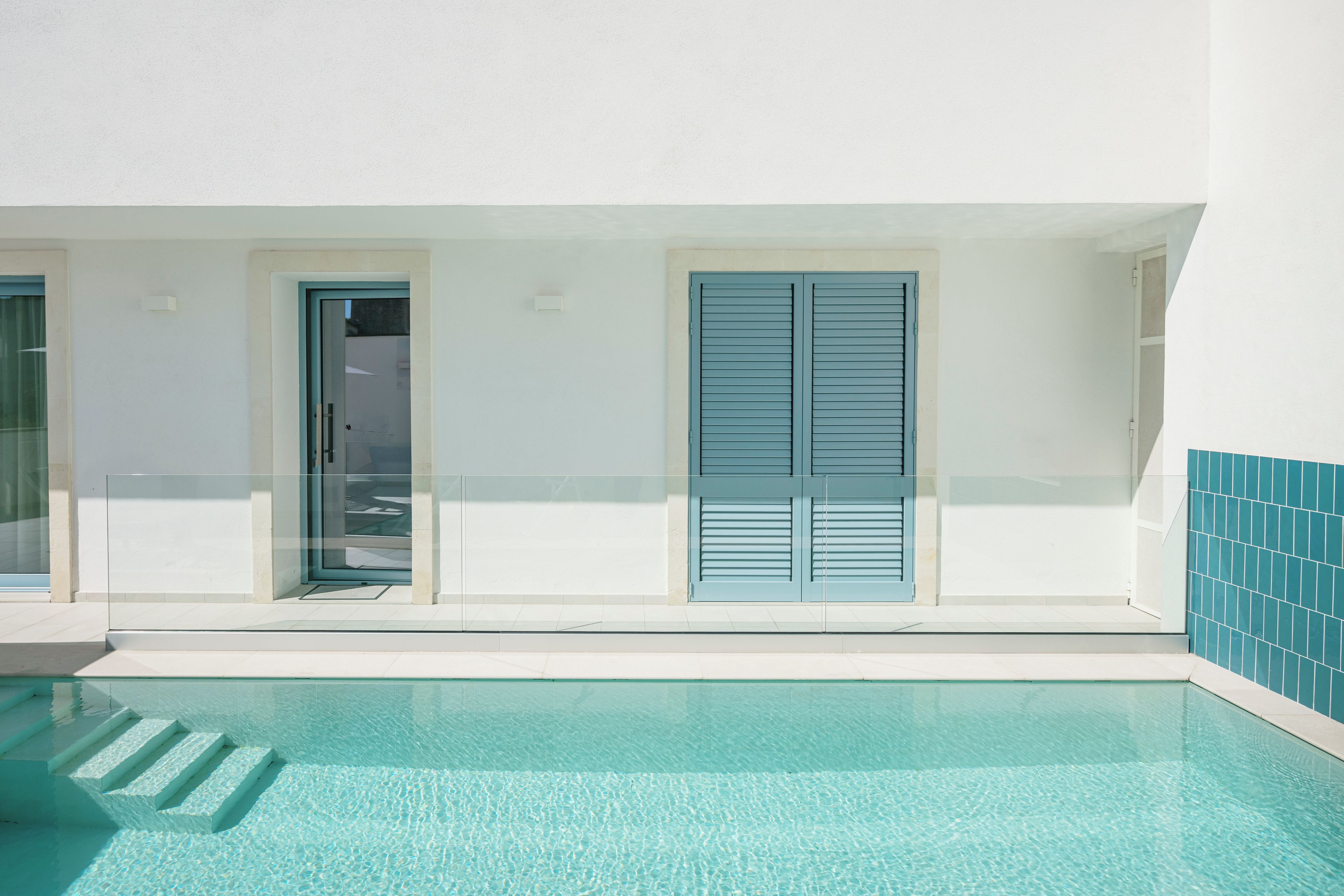 A modern building with a swimming pool, a door, and a window with shutters.