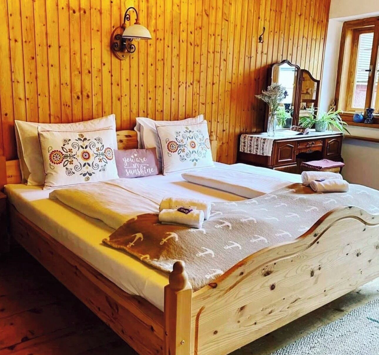 A wooden bed with a white bedspread, multiple pillows, and a nightstand with a lamp and a mirror.