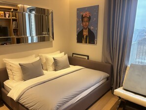 A bedroom with a bed, a bedside table, a chair, a bookshelf, and a painting on the wall. - Modern Flat, Moments from the Iconic Tower Bridge London Landmarks (London)