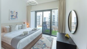 A modern hotel room with a large bed, a balcony with a view of buildings, a round mirror, and a small table with a yellow object. - PVH - Azizi Mirage 1 - Tranquil 1 BR (Dubai)