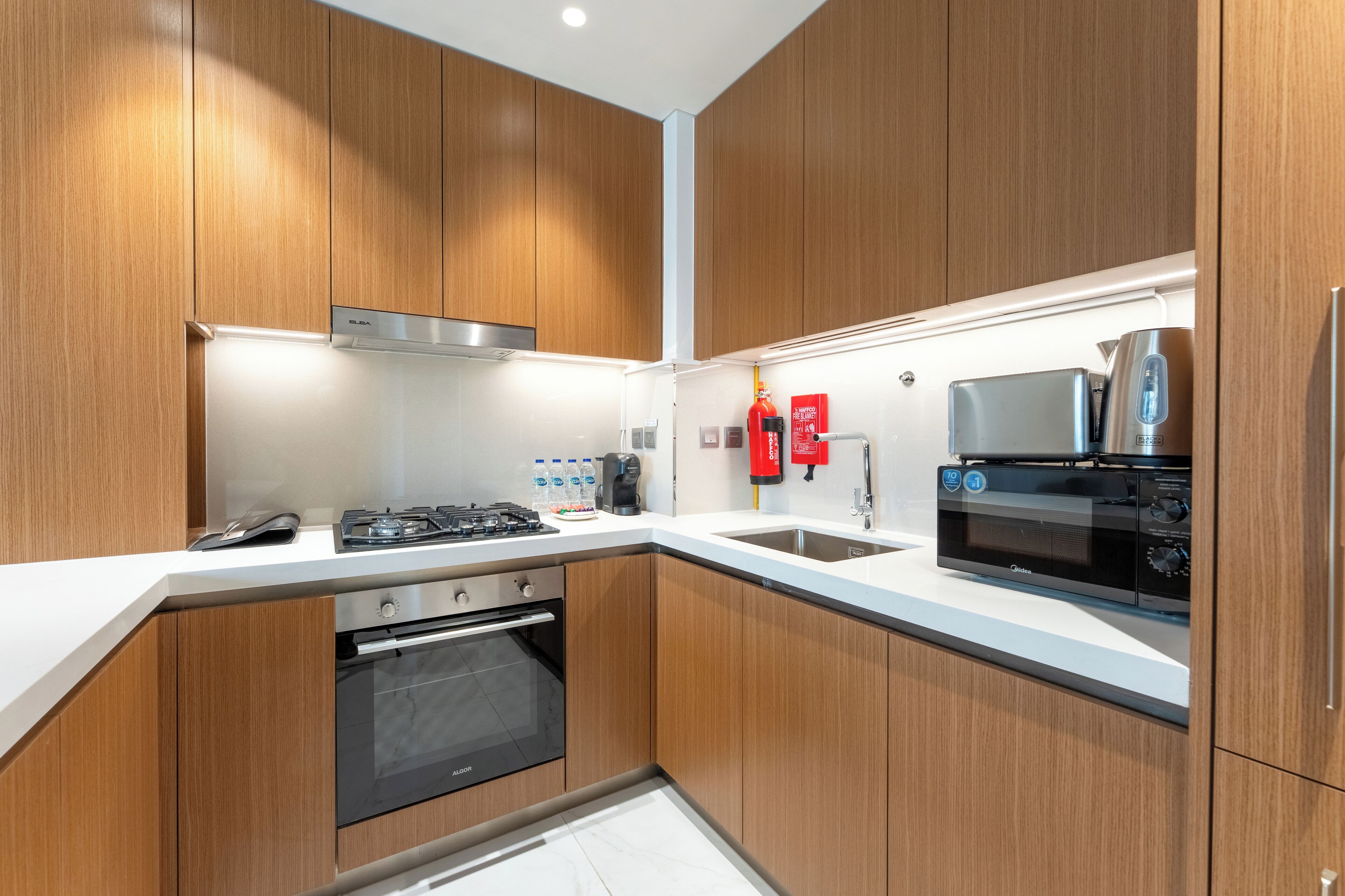 A modern kitchen with wooden cabinets, a stainless steel range hood, a built-in oven, a microwave, and a coffee machine.