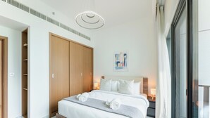 A modern hotel room with a large bed, wooden wardrobe, and a view through a sliding door. - PVH - Azizi Mirage 1 - Tranquil 1 BR (Dubai)