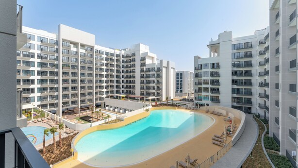 A modern apartment complex with a central swimming pool surrounded by lounge chairs and sunbeds. - PVH - Azizi Mirage 1 - Tranquil 1 BR (Dubai)