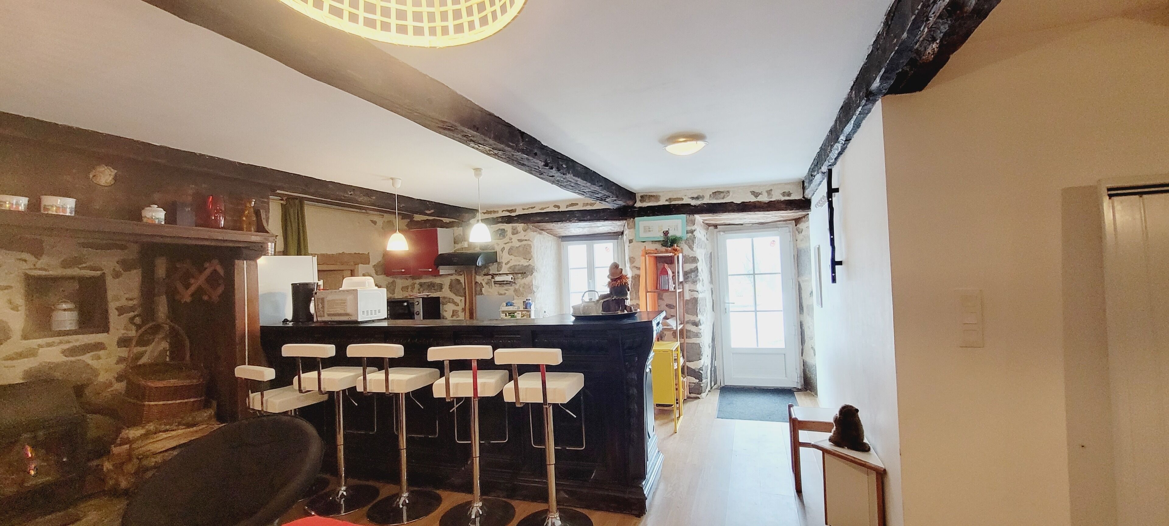 A rustic kitchen with a stone wall, wooden beams, and a bar area with stools.