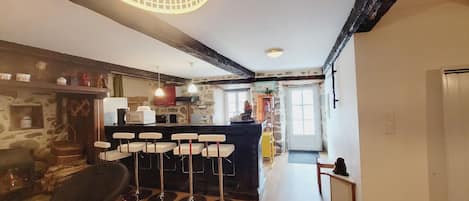 A rustic kitchen with a stone wall, wooden beams, and a bar area with stools.