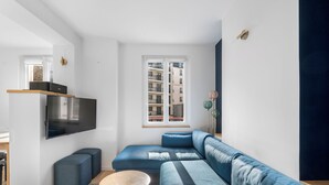 Een moderne woonkamer met een hoekbank, een flatscreen televisie en een kleine ronde tafel.