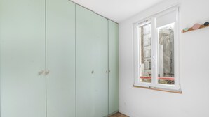 Een kamer met een lichtgroene garderobe, een raam met uitzicht op gebouwen en een houten vloer.