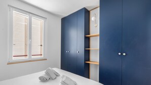 Een slaapkamer met een bed, twee opgerolde handdoeken, een kledingkast en een raam met jaloezieën.