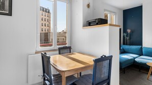 Een knus woongedeelte met een eettafel, stoelen, een blauwe bank en een klein bijzettafeltje.