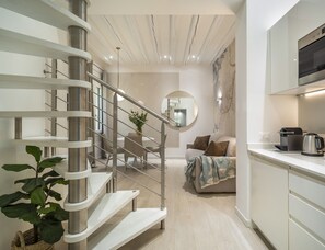 Een modern interieur met een spiltrap, een ronde spiegel, een bank met plaid en een keukenhoek met waterkoker.