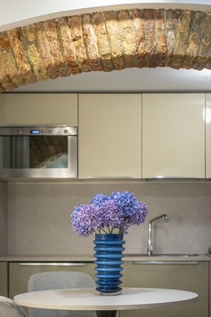 Eine Küche mit einem Steingewölbe, einem Edelstahlbackofen und einer Tischvase mit violetten Blumen.