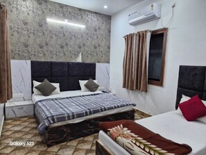 Une chambre avec un grand lit, un lit plus petit, une table de chevet, un appareil de climatisation et une fenêtre avec des rideaux.