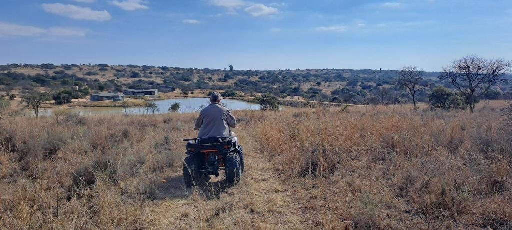 A person riding an ATV in a dry grass field with a lake and buildings in the background.