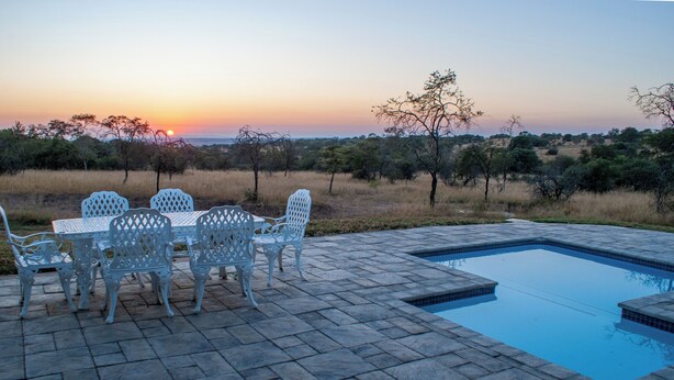 A pool with a view of the sunset, surrounded by a patio with chairs and a table. - Casa de la Presa 2 (Polokwane)