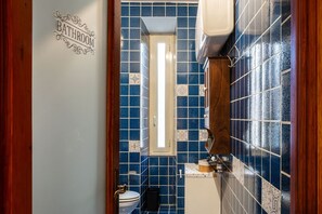 A bathroom with blue tiles, a white toilet, a wooden cabinet, and a 'BATHROOM' sign on the wall. - GuestHost - Cozy 90m2 apartment, perfect for 4 people, located on the ground floor of a typical building with cloister.The accommodation is located in the Re di Roma/San Giovanni district, a lively and central residential and commercial area.The city's (Rome)