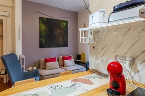 A living room with a sofa, a table, a red appliance, and a kitchen area with a microwave. - GuestHost - Cozy 90m2 apartment, perfect for 4 people, located on the ground floor of a typical building with cloister.The accommodation is located in the Re di Roma/San Giovanni district, a lively and central residential and commercial area.The city's (Rome)