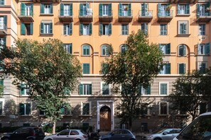 A multi-story building with balconies, a central entrance, and parked cars. - GuestHost - Cozy 90m2 apartment, perfect for 4 people, located on the ground floor of a typical building with cloister.The accommodation is located in the Re di Roma/San Giovanni district, a lively and central residential and commercial area.The city's (Rome)