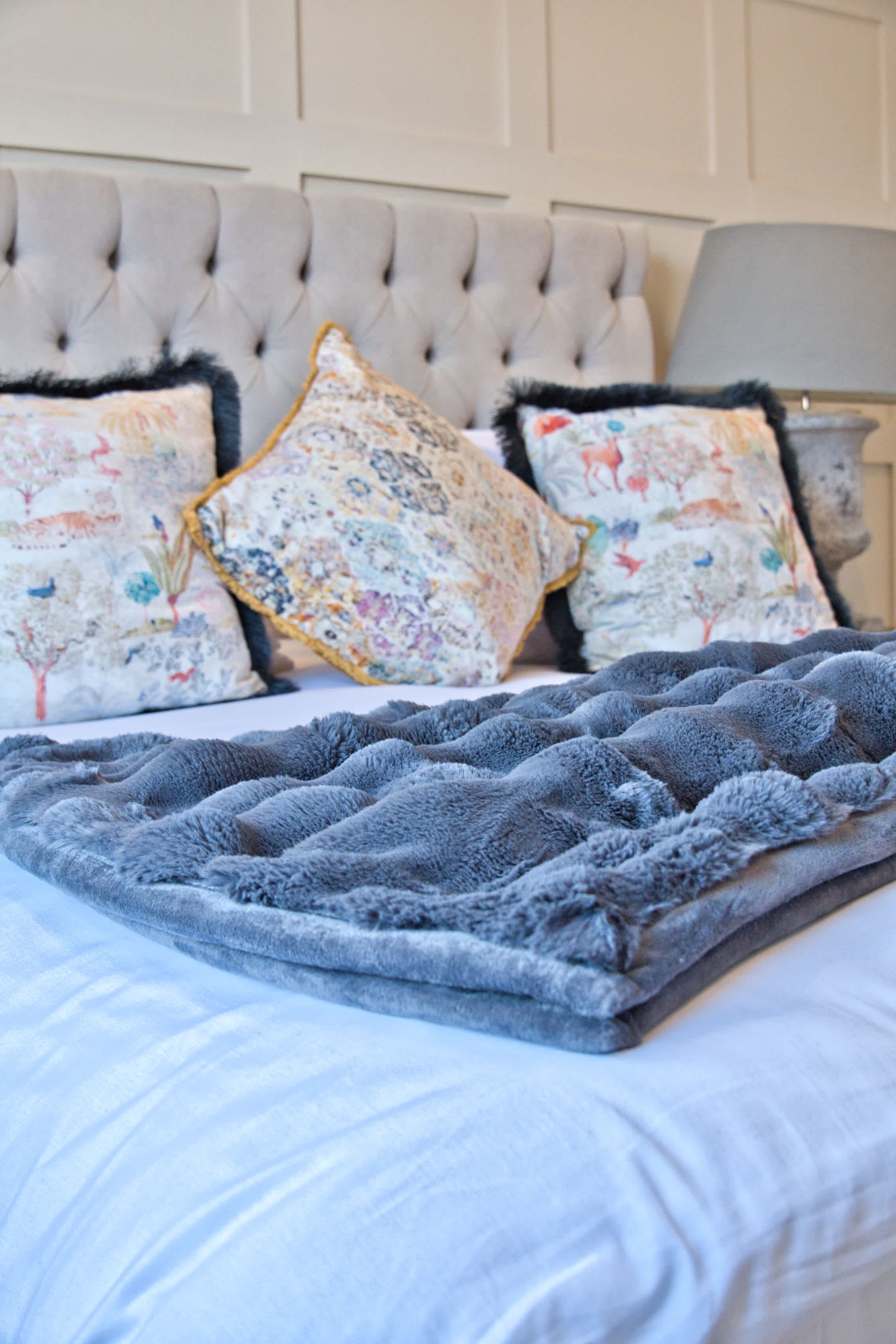 A bed with a tufted headboard, floral-patterned pillows, and a grey blanket.