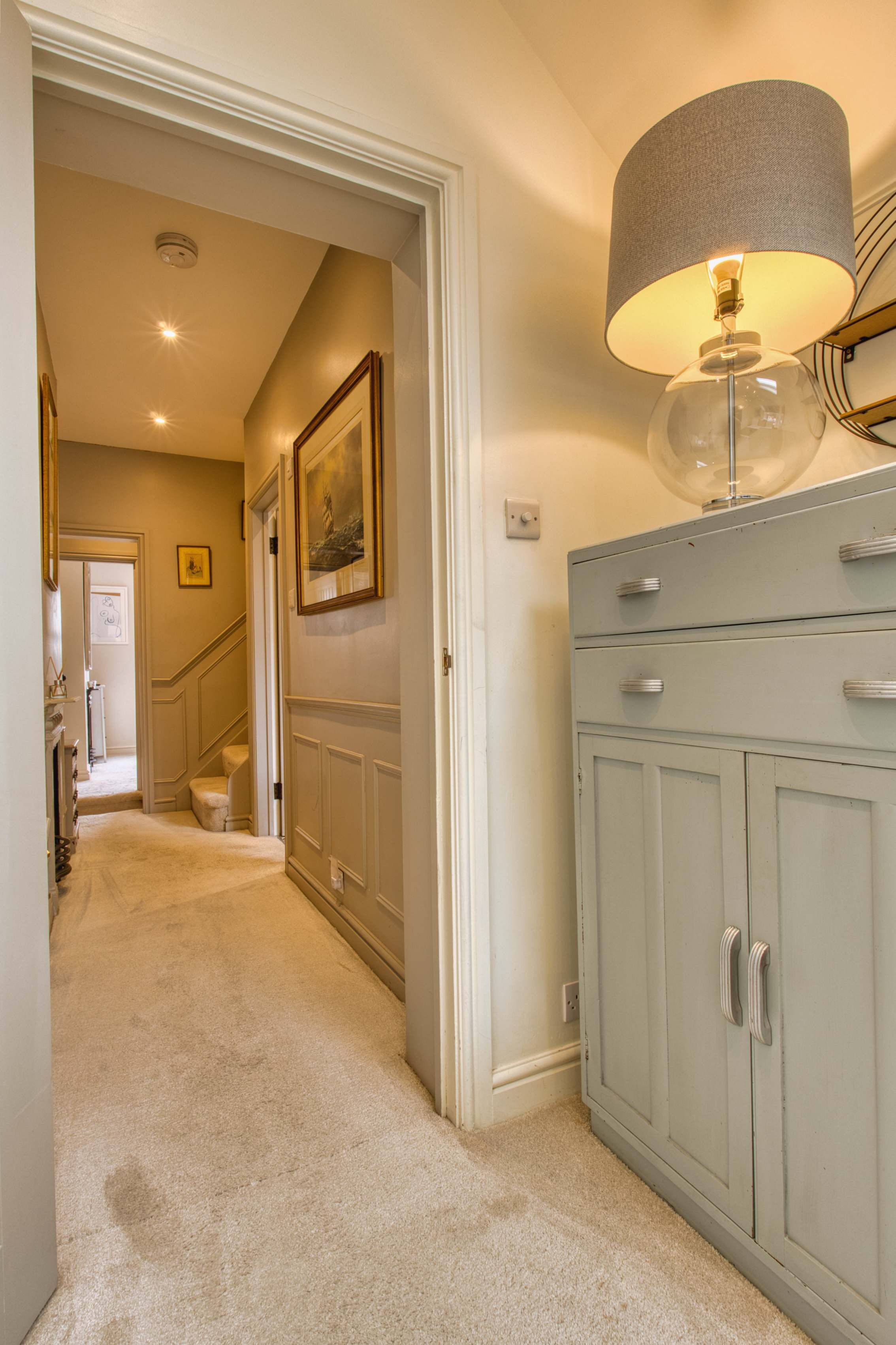 A hallway with a light blue cabinet, a lamp with a grey shade, and a framed picture on the wall.
