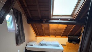 A loft bedroom with a skylight, wooden beams, a bed, a fluffy rug, and a window. - Detached chalet 100m2 open view (Xonrupt-Longemer)