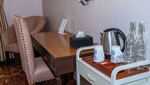 Ett hotellrum med ett skrivbord i trä, en bekväm stol, en minibar och en telefon som är monterad på väggen.