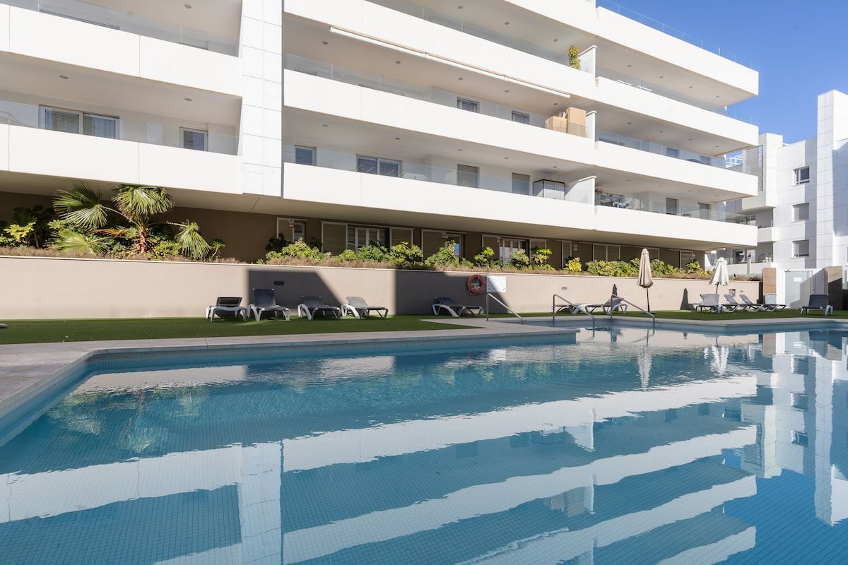 Et moderne hotel med swimmingpool, flere balkoner og liggestole.