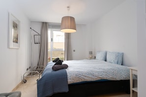A bedroom with a bed, a bedside table, a lamp, a window with curtains, and a floor lamp. - Acqua by Time & Home (San Pedro de Alcántara)