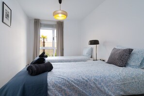 Habitación de hotel con dos camas, una ventana con cortinas, una lámpara de pie y un cuadro en la pared.