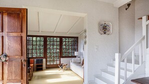 Een ruime kamer met een houten deur, een witte trap en een groot raam met uitzicht op groen.