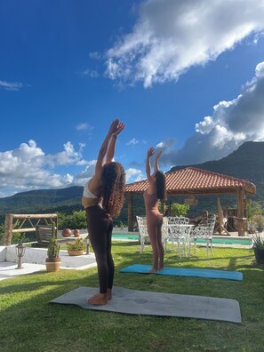Two people practicing yoga outdoors with a pool and dining area in the background.