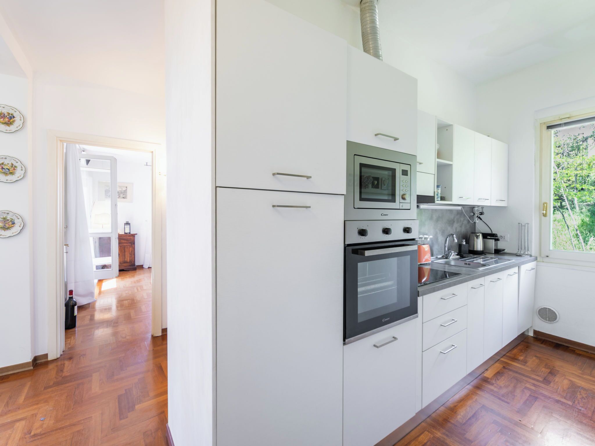 A modern kitchen with white cabinets, a built-in oven, microwave, and a stainless steel sink.