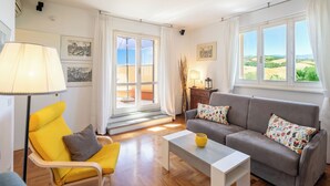 Een woonkamer met een bank, fauteuil, salontafel en uitzicht door een glazen deur.