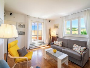 Ein Wohnzimmer mit Sofa, Sessel, Couchtisch und Blick durch eine Glastür.