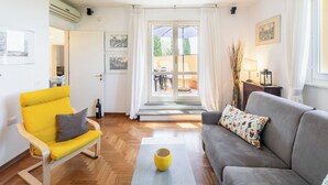 Een moderne woonkamer met een gele stoel, een grijze bank en een glazen deur naar een buitenruimte.