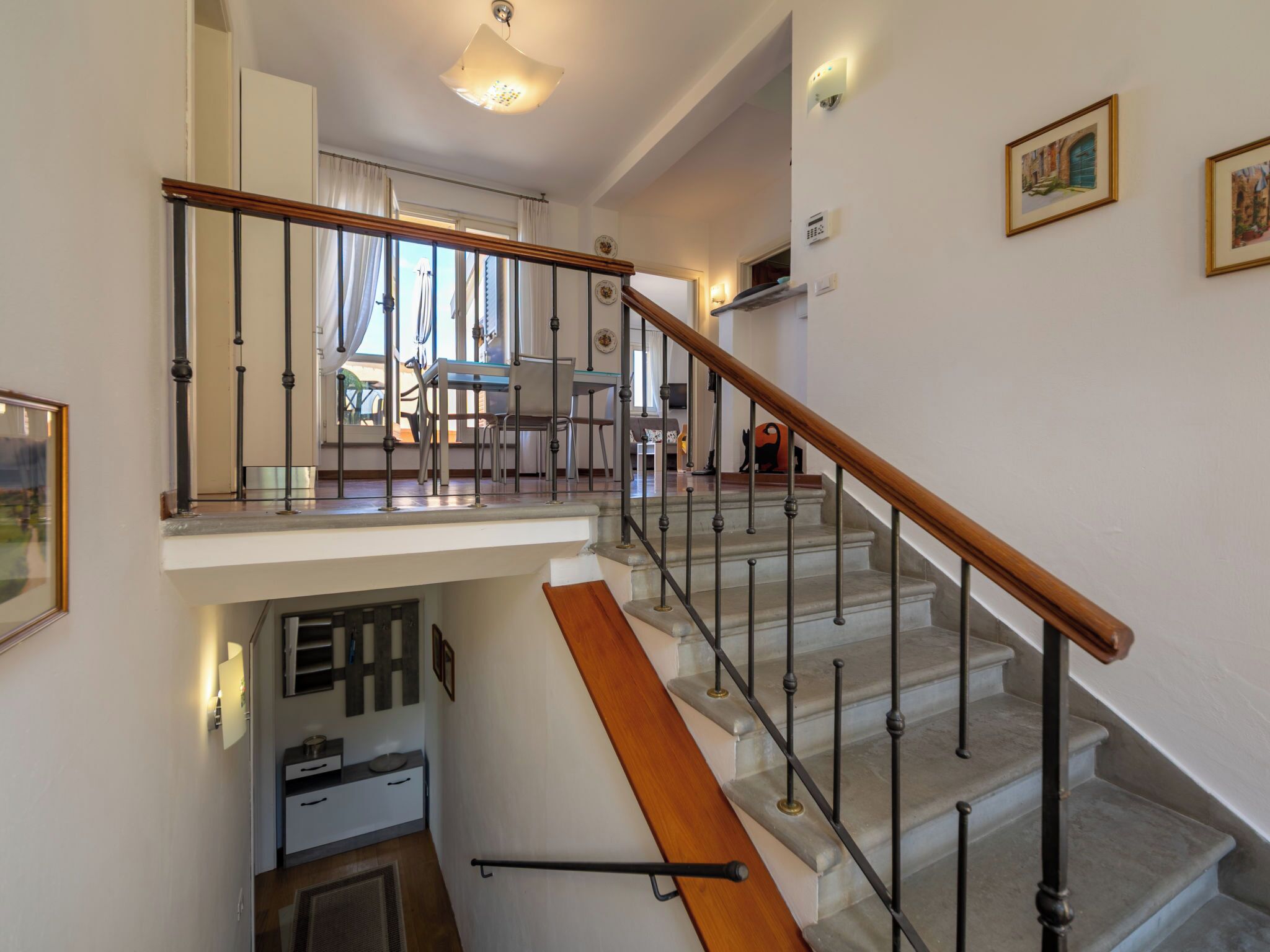 A staircase with a wooden handrail and metal balusters, leading to a dining area with chairs and a table.