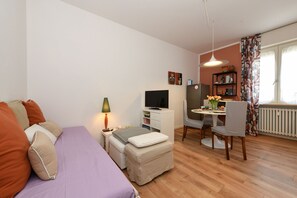 A compact room with a bed, a desk, a chair, and a TV. - Garden Apartment Bardolino - Coral Apartment (Bardolino)