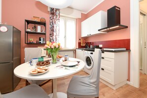 A compact kitchen with a dining area, a washing machine, and a refrigerator. - Garden Apartment Bardolino - Coral Apartment (Bardolino)