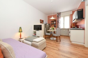 A compact living space with a bed, a desk, a chair, a television, and a kitchenette. - Garden Apartment Bardolino - Coral Apartment (Bardolino)